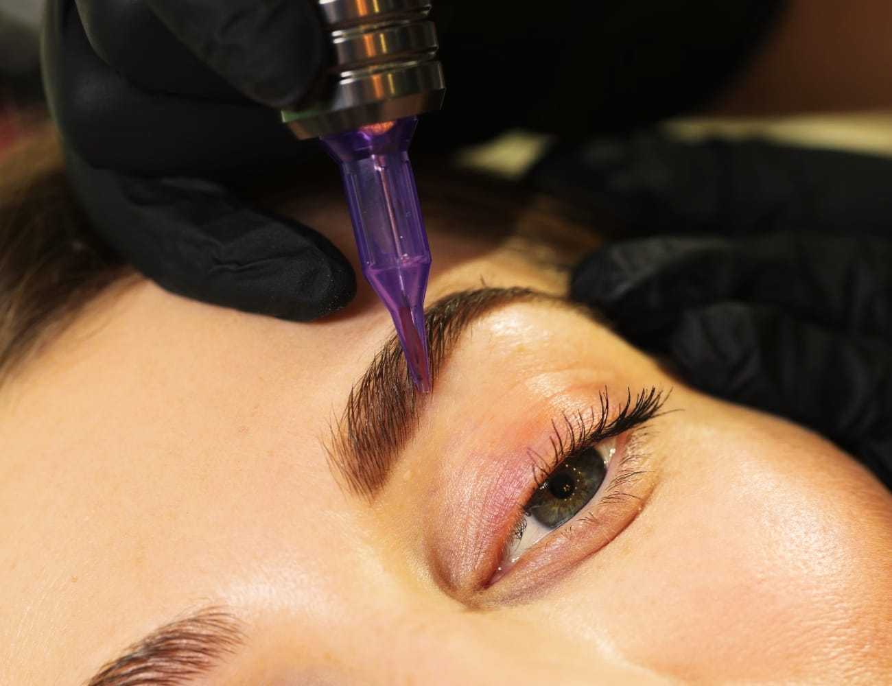 Close-up of a person receiving eyebrow microblading with a purple tool.
