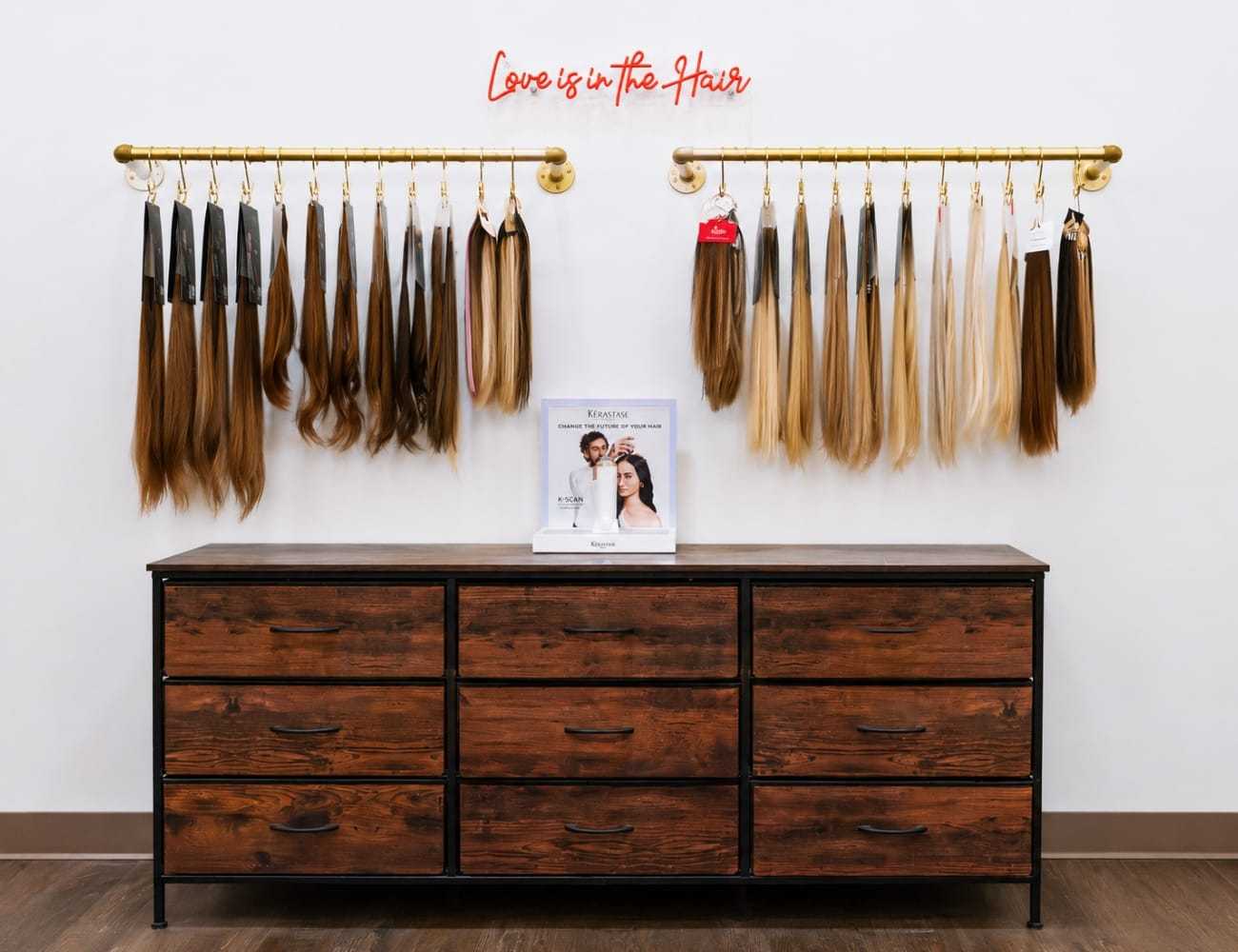 Hair extensions on display racks above a wooden dresser in a salon.