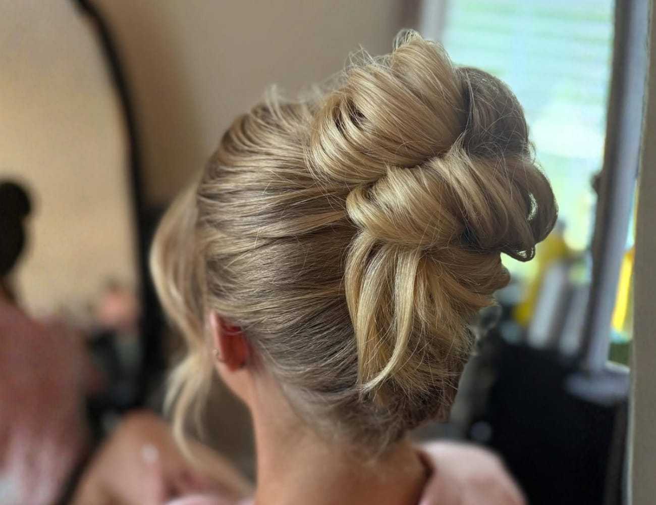 Elegant updo hairstyle with blonde hair in a bun, viewed from the back inside a room.