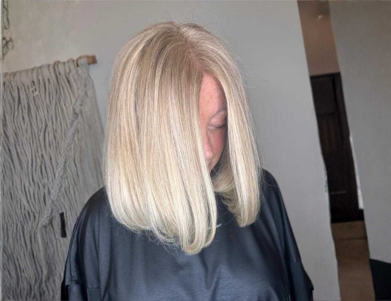 Short-haired woman with blond bob, looking down, in a salon setting.